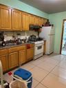 Kitchen featuring white gas stove, brown cabinetry, range hood, and light tile patterned floors