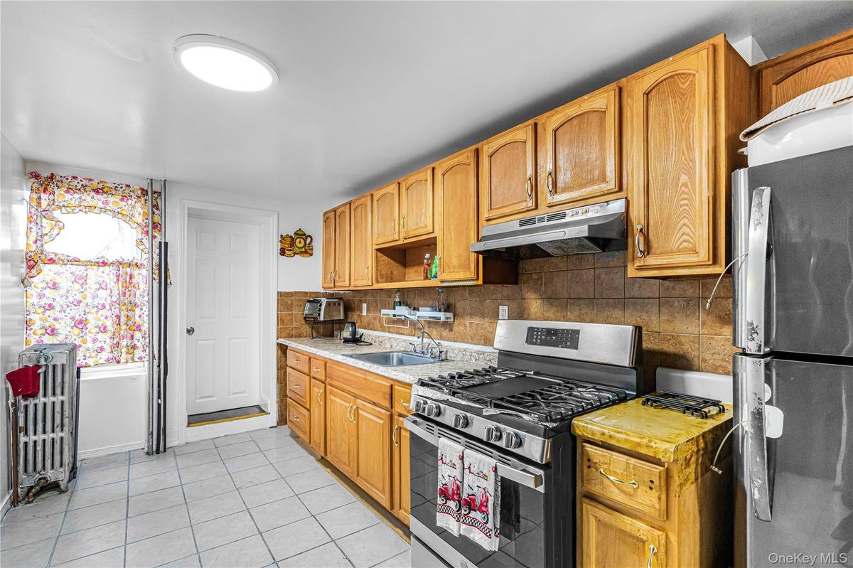Kitchen featuring light wood cabinetry, stainless steel range with overhead ventilation, and a tiled backsplash