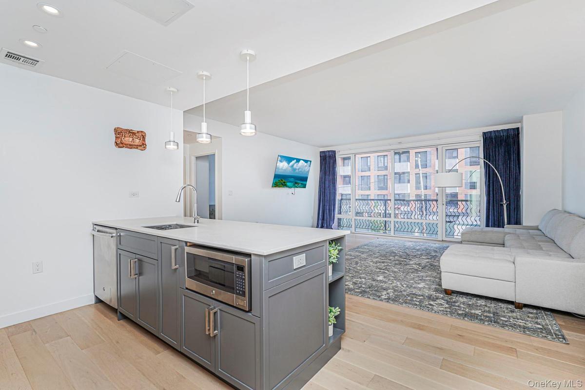 Kitchen with open floor plan, light wood-type flooring, hanging light fixtures, appliances with stainless steel finishes, and gray cabinetry