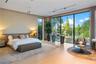 Spacious primary bedroom with wide-plank light wood floors, upholstered king headboard, leather bench, floor-to-ceiling sliding glass doors, direct wa