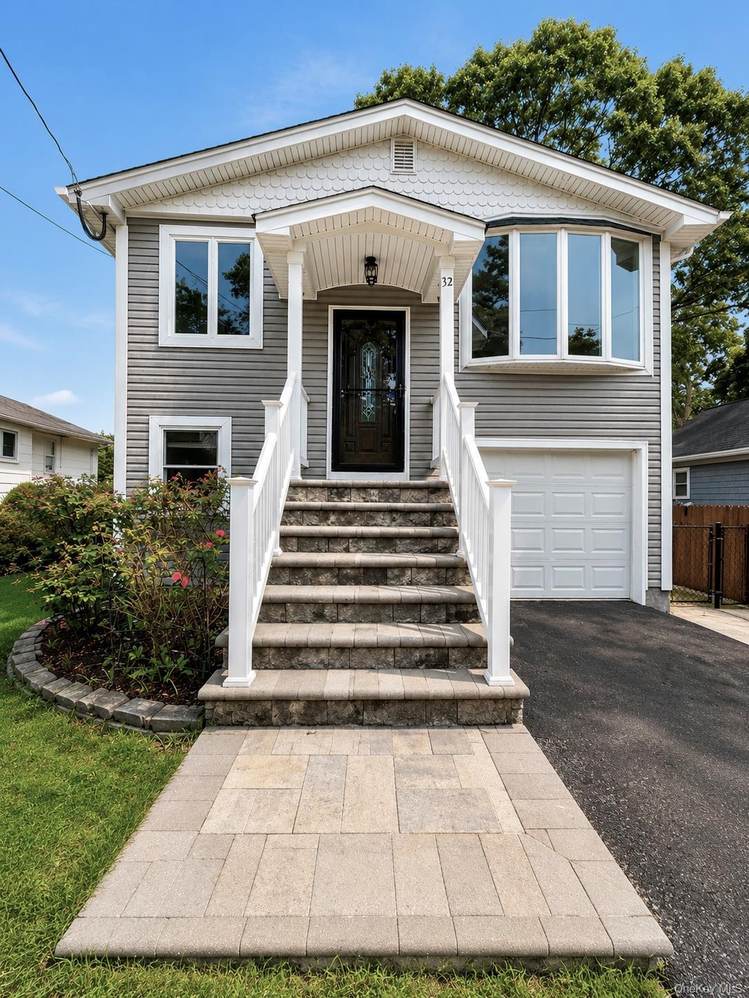 Exterior featuring gray siding, a covered entry porch, a bay window, and an attached garage with a white door.