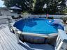 Expansive deck with an above-ground pool, featuring a white privacy fence and mature trees