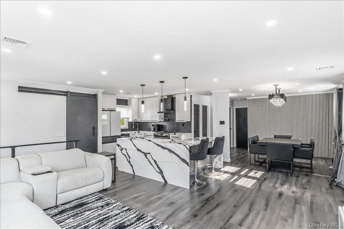 Open-concept living area featuring wood-finish flooring, a kitchen island with stone-finish waterfall countertop, recessed lighting, a modern barn doo