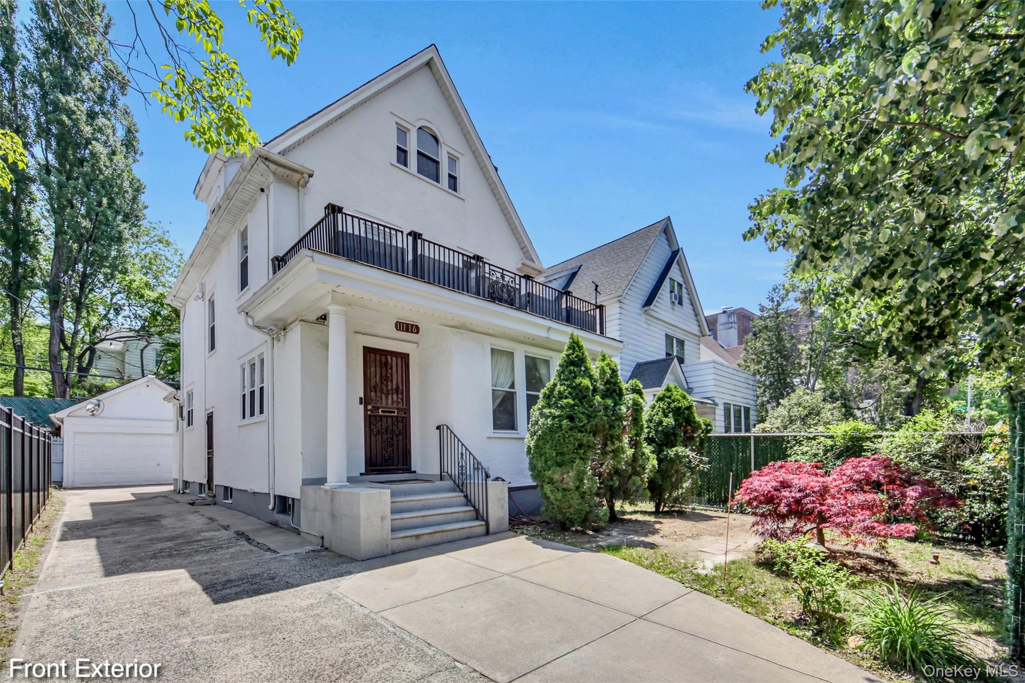 White stucco exterior with a covered front porch featuring two columns and a second-story balcony with metal railings