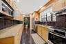 Galley kitchen featuring light wood cabinetry, stone countertops, stainless steel appliances, and a dark stone backsplash