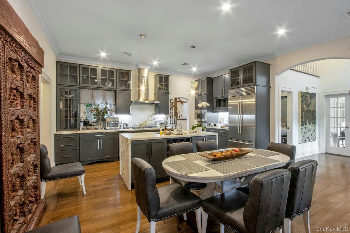 Kitchen with appliances with stainless steel finishes, a kitchen island with sink, wall chimney range hood, pendant lighting, and light hardwood / woo