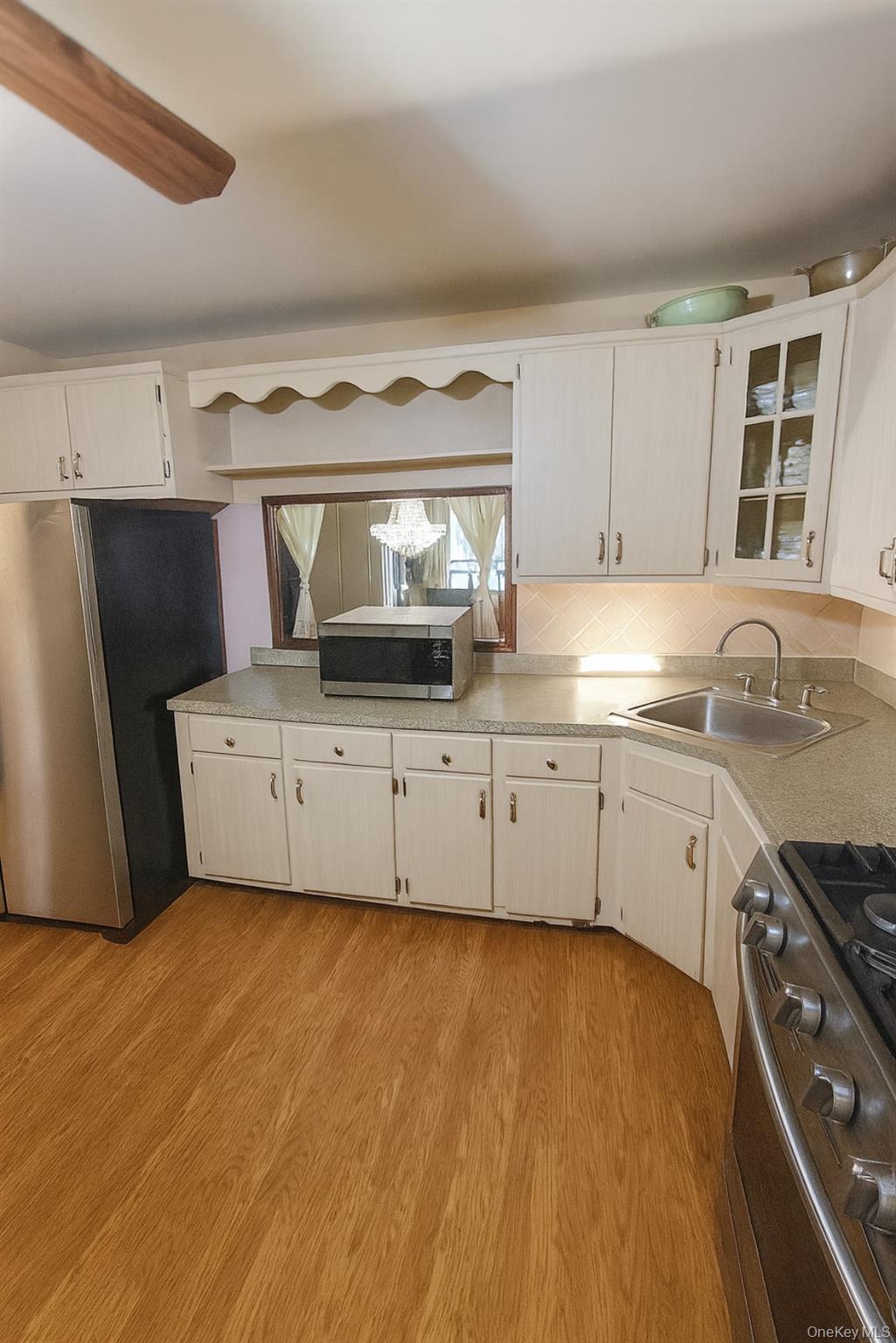 Kitchen featuring appliances with stainless steel finishes, light countertops, light wood-type flooring, glass insert cabinets, and white cabinetry