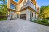 Wide paver motor court with glass-panel garage door, stone and stucco facade, spiral topiaries, recessed entry portico with wood-plank ceiling, circul