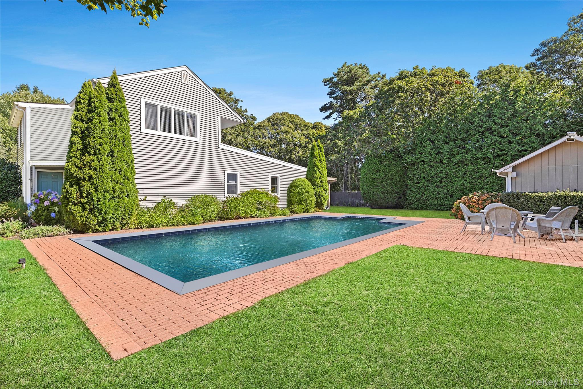 Outdoor pool with a patio area, a lawn, and view of wooded area