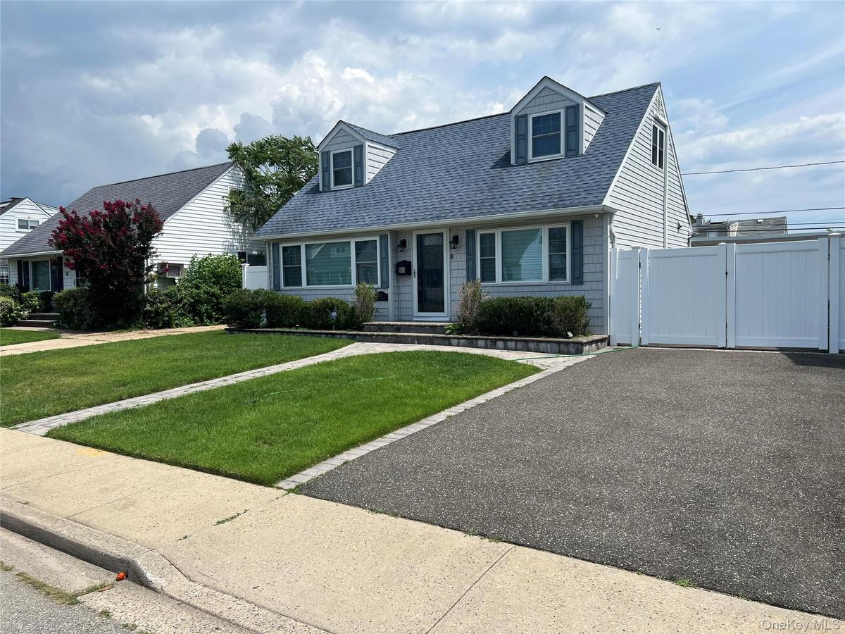 Classic Cape Cod home featuring a freshly sealed asphalt driveway, manicured lawn with defined landscaping borders, large picture windows with dark tr