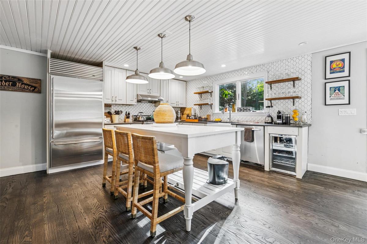 Kitchen with open shelves, hanging light fixtures, appliances with stainless steel finishes, and decorative backsplash