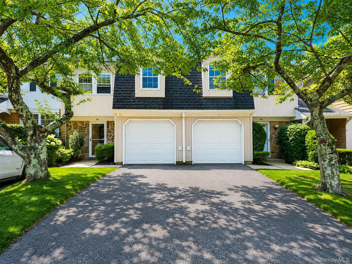 Exterior featuring a dark shingle roof, light-colored siding, stone accents, two white garage doors, and a paved driveway
