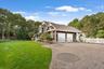 View of side of property with decorative driveway, view of scattered trees, a shingled roof, and a garage