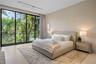 Bright en-suite bedroom with upholstered king bed, matching nightstands with table lamps, neutral textured walls, light stone floors, area rug, sheer