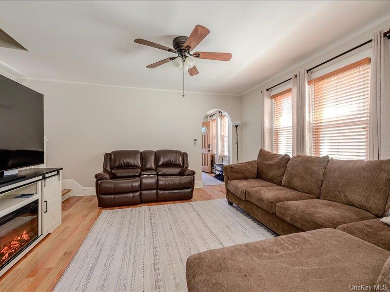 Living area featuring wood-finish flooring, a ceiling fan with light fixture, and archway entry
