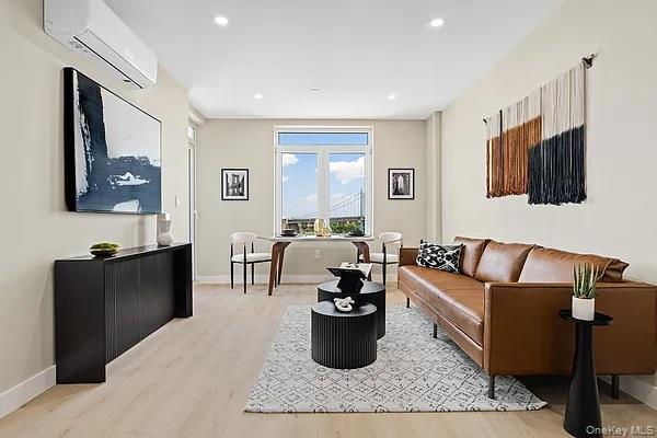 Living area with an AC wall unit, light wood-style floors, and recessed lighting