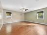 Hardwood flooring, ceiling fan, window-mounted air conditioning unit, and multiple windows with roller shades
