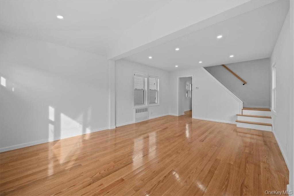 Unfurnished living room featuring light wood-style floors, stairway, recessed lighting, and radiator