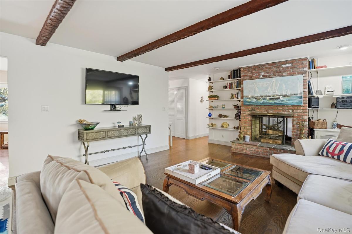Living room with wood finished floors, a fireplace, beamed ceiling, and built in shelves