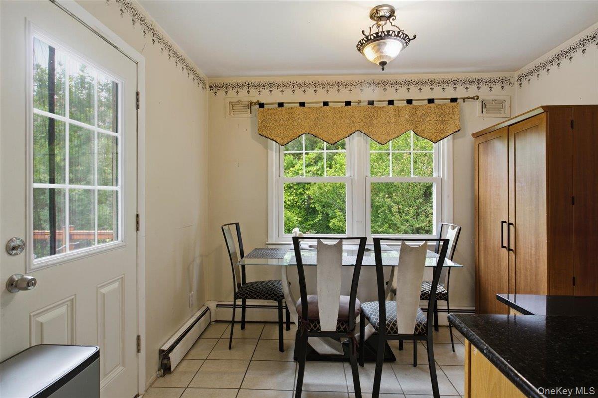 Kitchen dining area featuring a glass-paned door, double windows, tiled flooring, built-in baseboard heating, and a flush-mount ceiling light fixture