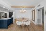Dining area with a custom octagonal hardwood table, brass-and-glass chandelier, navy kitchen island in the background, and a panel-board accent wall.