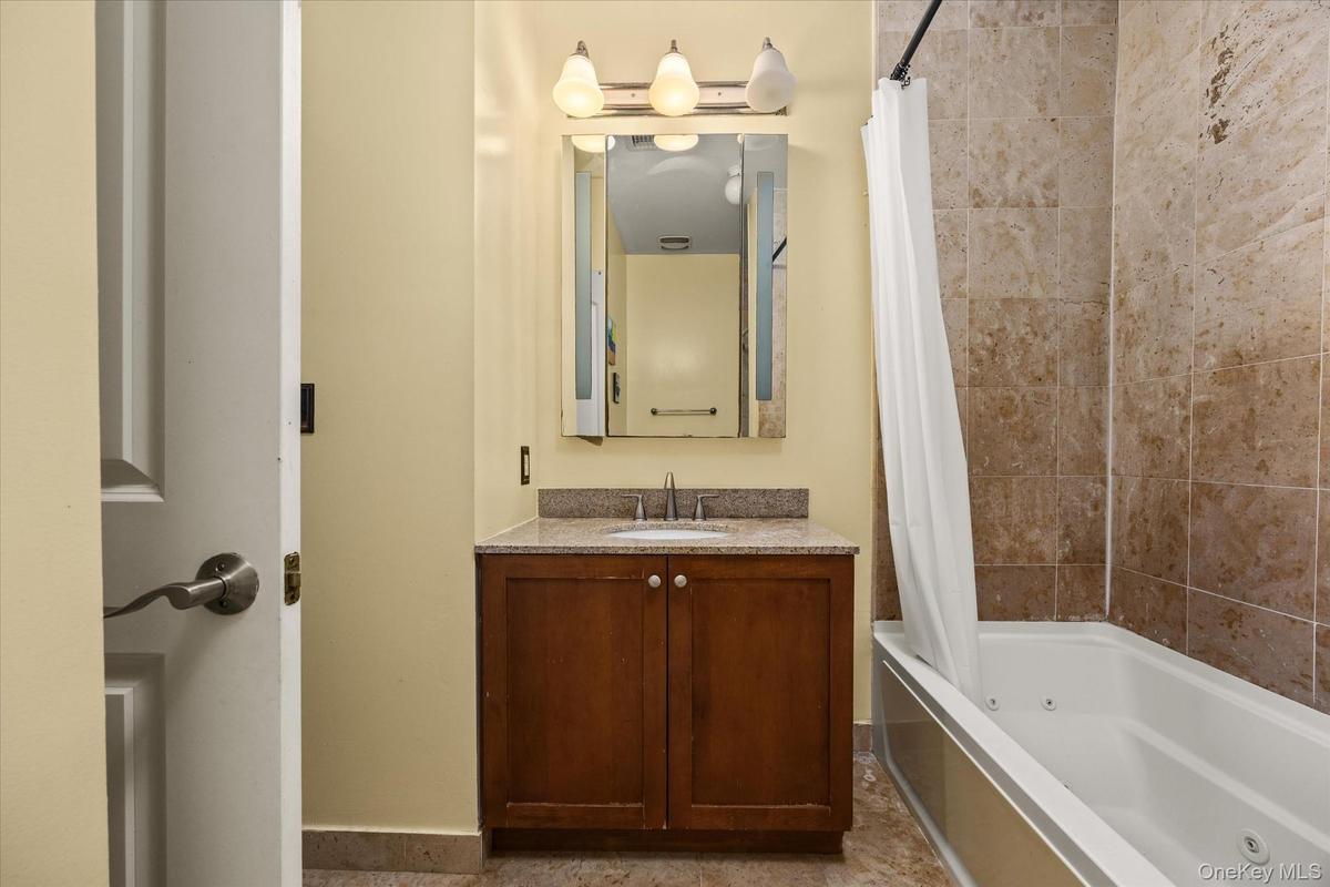 Bathroom featuring a wood vanity with a light-toned countertop, an integrated sink, and a wall-mounted mirror with overhead lighting