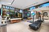 Full private wellness center with curved treadmill, massage table, yoga mats, kettlebells, wall-mounted TV, full-wall mirror, light wood floors, track