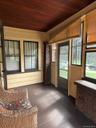 Enclosed porch featuring dark wood-finish flooring, a wood-paneled ceiling, multiple windows with dark frames, and a partial brick wall element