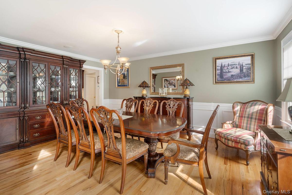 Dining area featuring a chandelier, ornamental molding, light wood-style floors, wainscoting, and a decorative wall