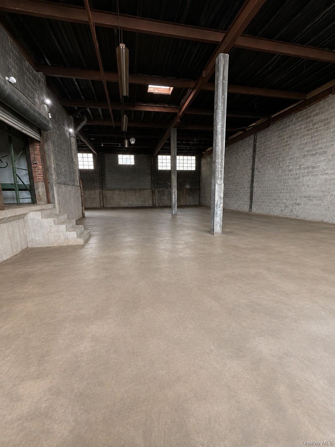 Expansive open-concept space featuring exposed structural beams, a concrete floor, and block walls