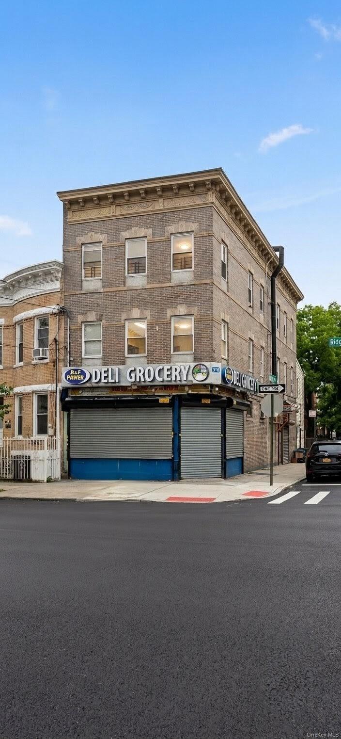 Three-story brick building featuring ground-floor commercial space with roll-down security gates and upper-level windows