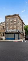 Three-story brick building featuring ground-floor commercial space with roll-down security gates and upper-level windows