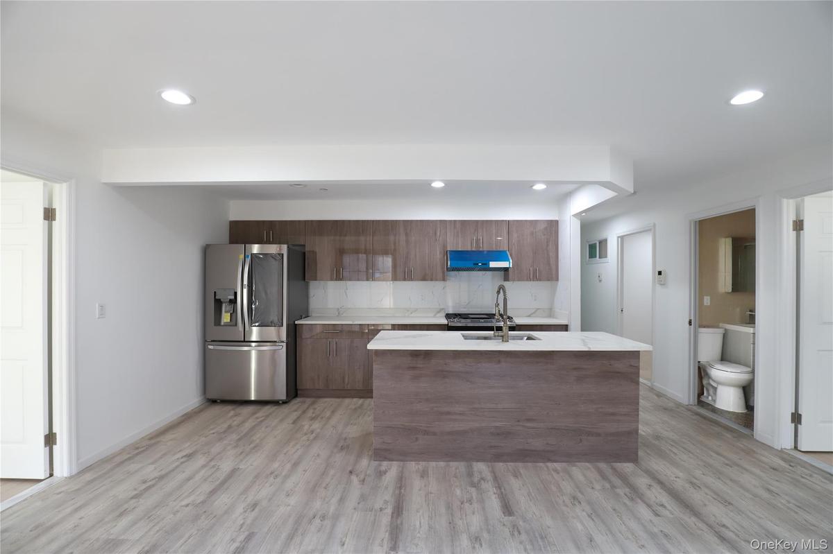 Kitchen with stainless steel fridge with ice dispenser, an island with sink, light wood-type flooring, tasteful backsplash, and recessed lighting
