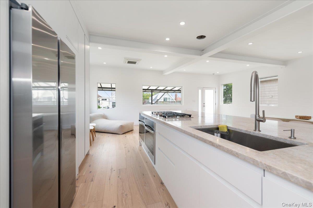 Kitchen with appliances with stainless steel finishes, light wood-style flooring, beamed ceiling, white cabinetry, and recessed lighting