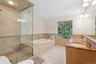 Full bathroom featuring wainscoting, double vanity, a stall shower, a bath, and tile walls