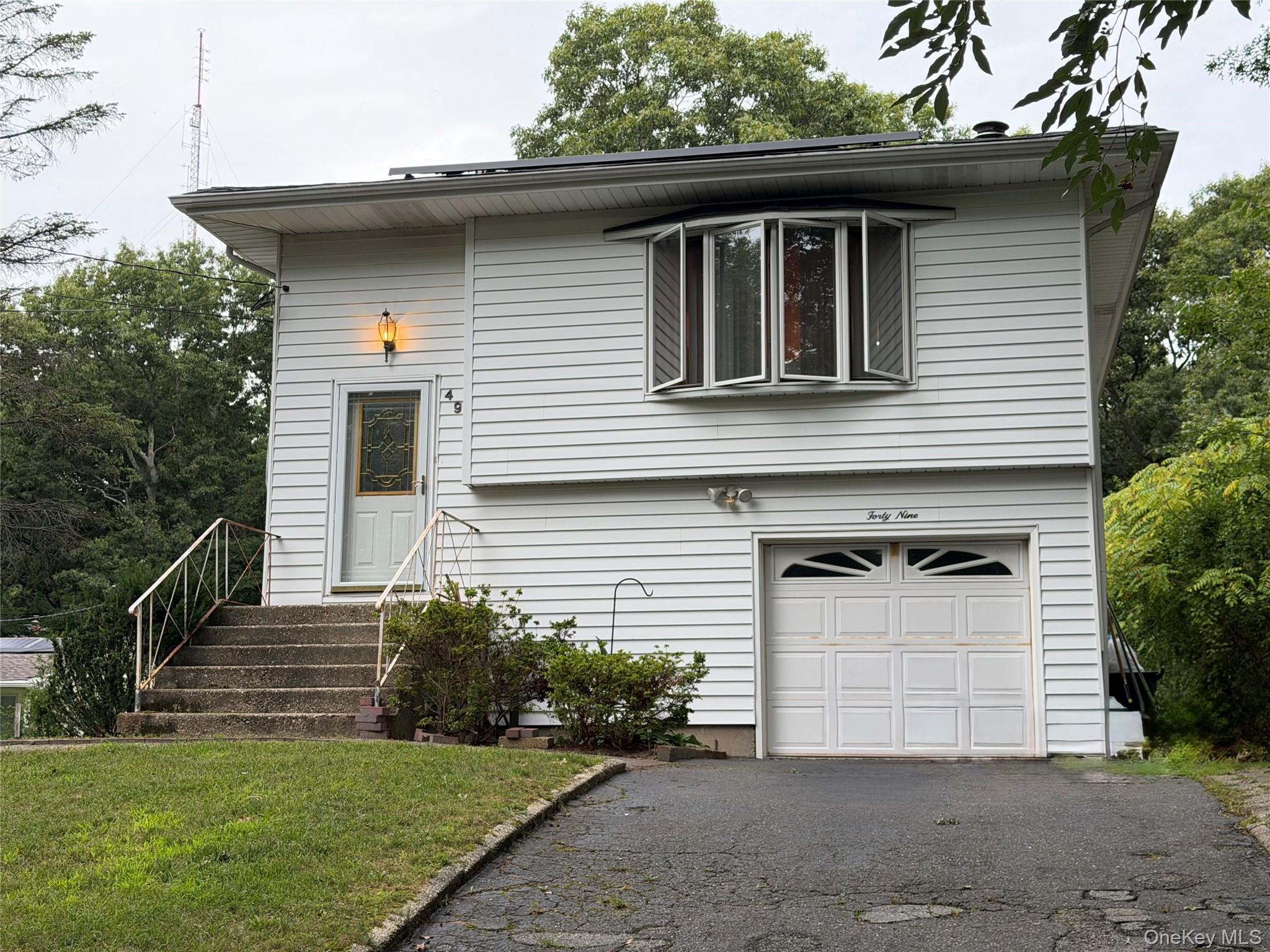 Exterior featuring white horizontal siding, a bay window with multiple panes, a white garage door with decorative lites, and a paved driveway