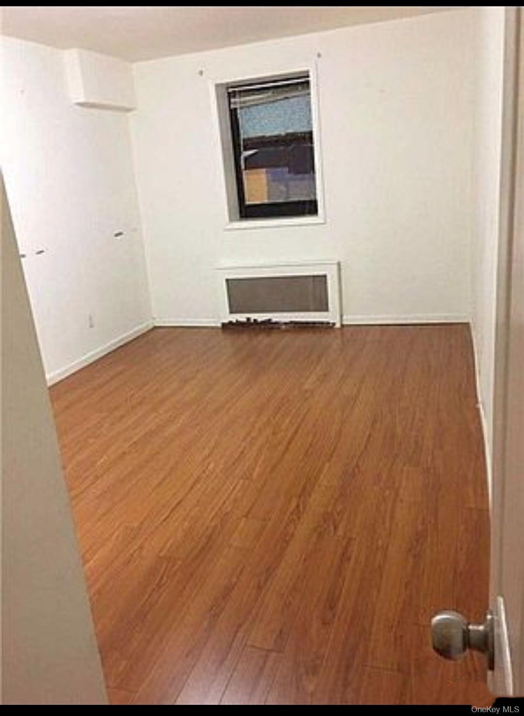 Empty room with dark wood-style floors and radiator heating unit