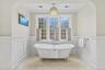 The primary suite offers a serene sanctuary centered around a classic clawfoot soaking tub framed by elegant wainscoting and a sprawling triple-window