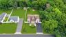 Expansive property featuring a multi-level residence with a brown shingle roof and white siding, an attached paved driveway, and a manicured lawn