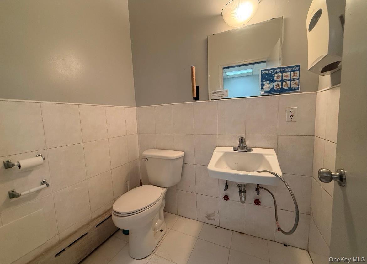 Bathroom featuring baseboard heating, sink, tile walls, tile patterned flooring, and toilet