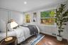 Newly renovated bedroom with warm hardwood floors and picture windows framing serene wooded views for a peaceful retreat.