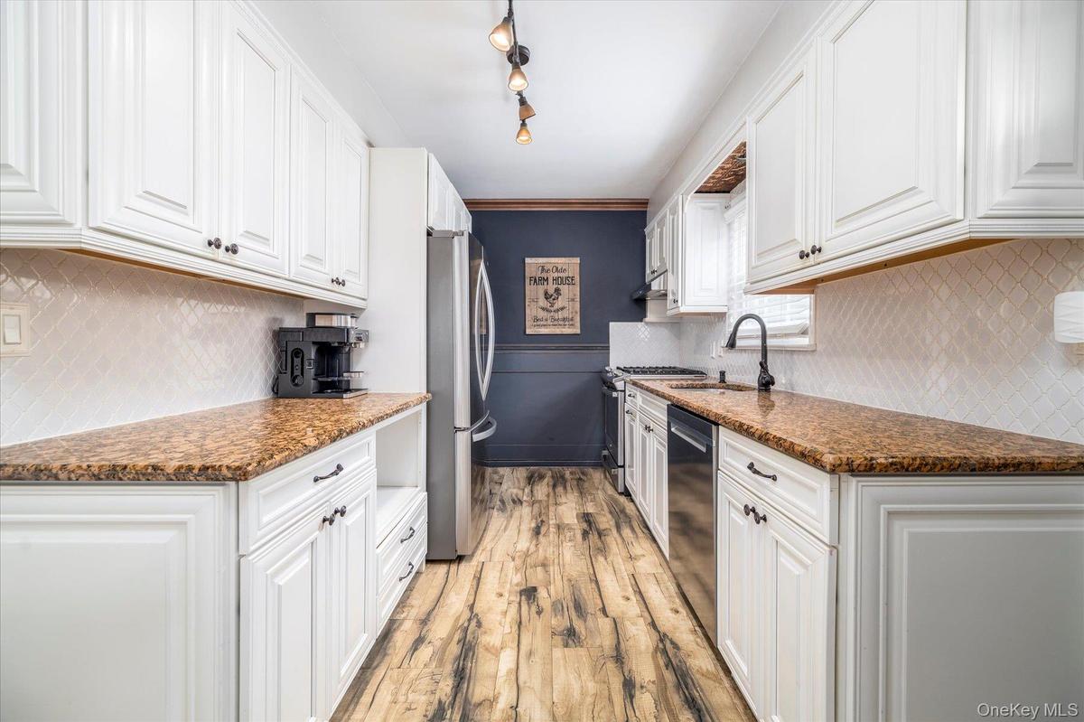 Renovated kitchen featuring white cabinetry, wood-finish flooring, and stone countertops