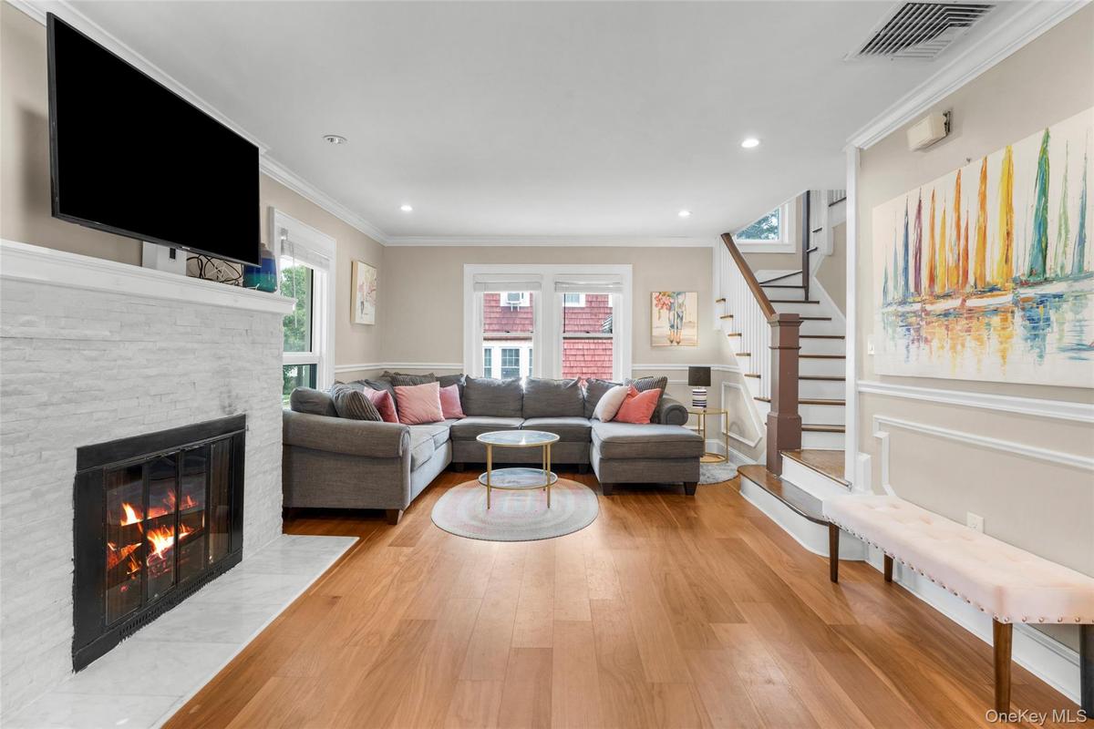 Spacious interior featuring wood-finish flooring, a white stacked stone fireplace, and crown molding, recessed lighting.