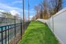 Grassed recreation area featuring a white privacy fence and black metal dog park fencing bordering a tennis court