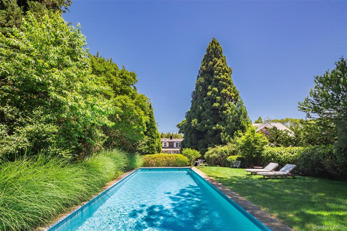 Rectangular swimming pool with a stone coping, surrounded by a lush green lawn and mature trees