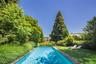 Rectangular swimming pool with a stone coping, surrounded by a lush green lawn and mature trees