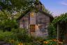 As evening falls, the wellness studio glows warmly amid mature gardens and lush landscaping